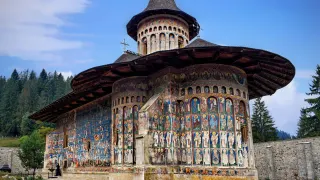 Biserica Mănăstirii Voroneț, cu frescele exterioare și dealurile împădurite ale Bucovinei